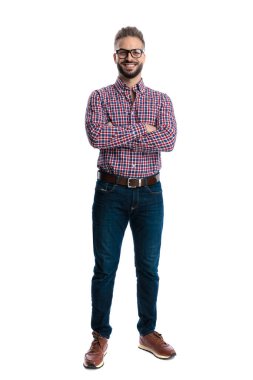 Gözlüklü ve ekose gömlekli rahat bir adam beyaz arka planda yalnız başına ileriye bakarken tüm vücudu çapraz kollarla ayakta duruyor.