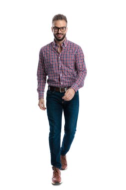 Gözlüklü ve ekose gömlekli mutlu bir adam beyaz arka planda gülümserken tüm vücudunu öne doğru yürüyor.