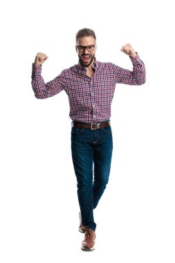 Heyecanlı, gözlüklü, kareli tişörtlü bir adam beyaz arka planda izole edilmiş kutlamada yumruklarını kaldırarak yürüyor ve ileriye bakıyor.