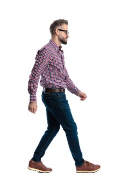 Gözlüklü, kareli tişörtlü, beyaz arka planda yürüyen ve ileriye bakan kararlı bir adamın yan görüntüsü