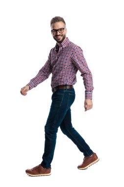 Gözlüklü, kareli tişörtlü mutlu bir adamın beyaz arka planda yürümesi ve ileriye bakması.
