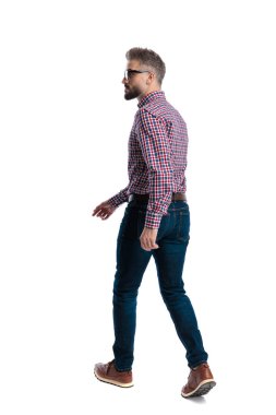 Beyaz arka planda kareli gömlek ve kot pantolon giyen kendine güvenen bir adamın yan görünüşü.