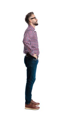 Ekose gömlek giyen ve gözlüklü mutlu bir adam elleri ceplerinde beyaz arka plana bakıyor.