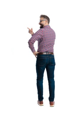 Ekose gömlek giyen, eli kalçasında duran ve beyaz arka planda parmağını sağa sola gösteren neşeli bir adam.