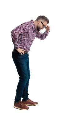 Üzerinde işaretli gömlek ve gözlük olan, alnında alnı olan, beyaz arka plana bakan stresli, sıradan bir adamın yan görüntüsü.