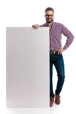 Gözlüklü ve ekose gömlekli mutlu bir adam beyaz arka planda ilerlerken elleri kalçasında büyük boş bir levhaya yaslanıyor.