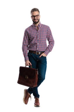 Gözlüklü, ekose gömlekli, deri çantalı neşeli bir adam beyaz arka planda bacak bacak üstüne atmış duruyor.