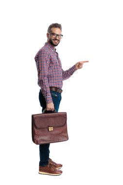 Gözlüklü, mutlu, sıradan bir adamın evrak çantasını tutarken diğer tarafı göstermesi ve beyaz arka planda izole bir şekilde ileriye bakması.