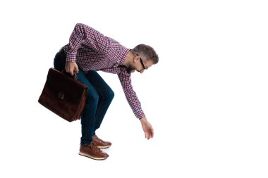 Meraklı sakallı bir adamın beyaz arka planda izole edilmiş deri evrak çantasını tutarken yere doğru eğildiğini ve uzandığını gördüm.