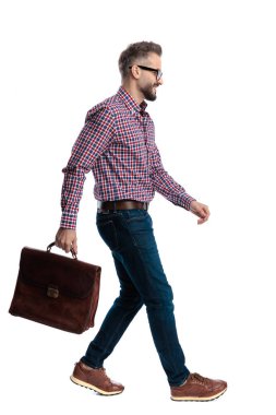 Deri çantayla yürüyen ve beyaz arka planda gülümseyen mutlu, zeki, sıradan bir adamın yan görüntüsü.