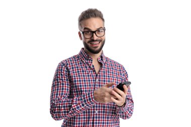 Ekose gömlekli ve gözlüklü mutlu bir adam akıllı telefon tutuyor ve beyaz arka planda soyutlanmış bir şekilde ileriye bakıyor.
