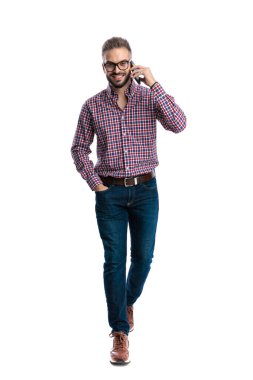 Neşeli, sıradan bir adam cep telefonuyla yürürken ve konuşurken beyaz arka planda ileriye bakıyor.