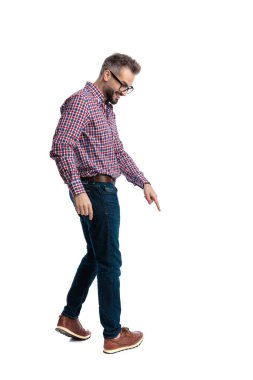 Gözlüklü, kareli tişörtlü, mutlu bir adamın yürüdüğünü, parmağını aşağı uzattığını ve beyaz arka plana baktığını görüyorum.