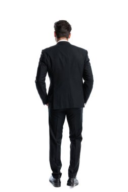 Beyaz arka planda elleri ceplerinde duran siyah takım elbiseli şık bir adamın arka planı.