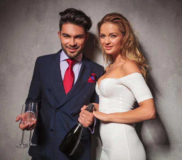 Lyckliga eleganta paret håller en flaska champagne och glas Stockbild