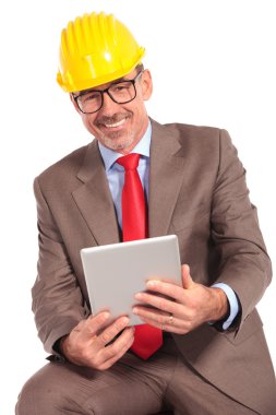 smiling old construction engineer holding a tablet pad and sitti