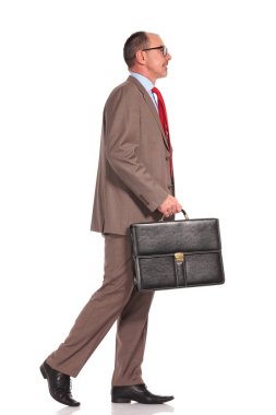 side view of a senior businessman holding suitcase and walking