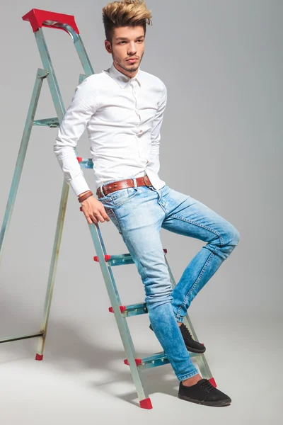 Joven posando en el fondo del estudio mientras sube en una escalera —  Fotos de Stock