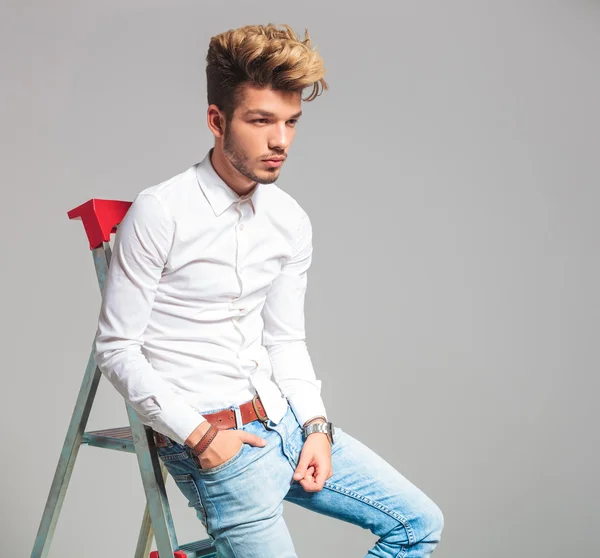 Man posing with hand in pocket while sitting on a ladder — Stock fotografie