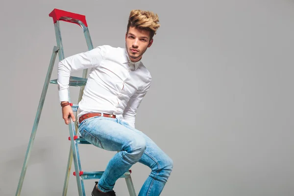 Fashionable young man sitting on a ladder while posing in studio — Stock fotografie