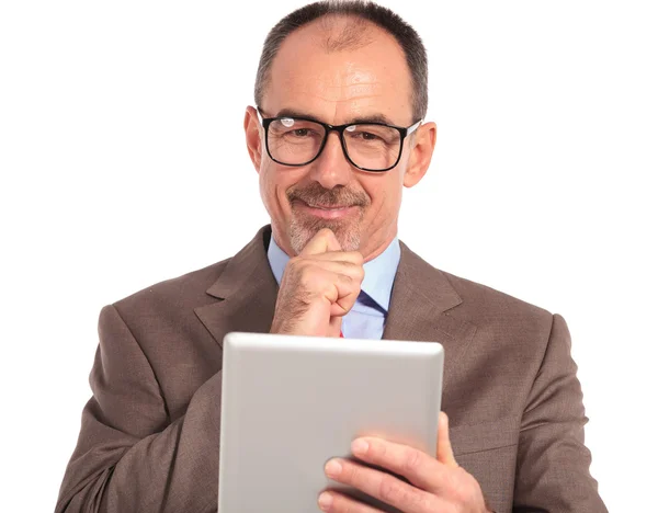 Улыбающийся задумчивый бизнесмен читает на планшете — стоковое фото