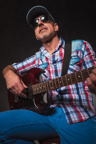 Senior man playing an electric guitar seated, looks up — Stock fotografie