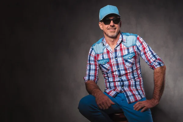 Viejo hombre casual con sombrero de béisbol y gafas de sol sentado — Foto de Stock