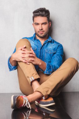 stylish man sitting in studio background legs crossed looking at