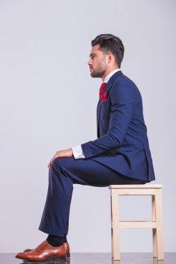 Studio elleriyle dizlerinin üzerinde oturan takım elbiseli adam