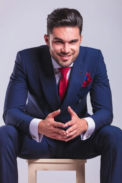 Man in suit sitting in studio smiling with palms touching — Stock Photo, Image