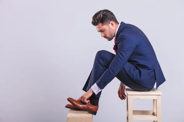 Человек в костюме, сидящий на стуле в студии, чистит обувь — стоковое фото