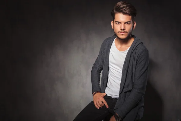 Hombre posando en el estudio con la mano en el bolsillo mientras está sentado — Foto de Stock