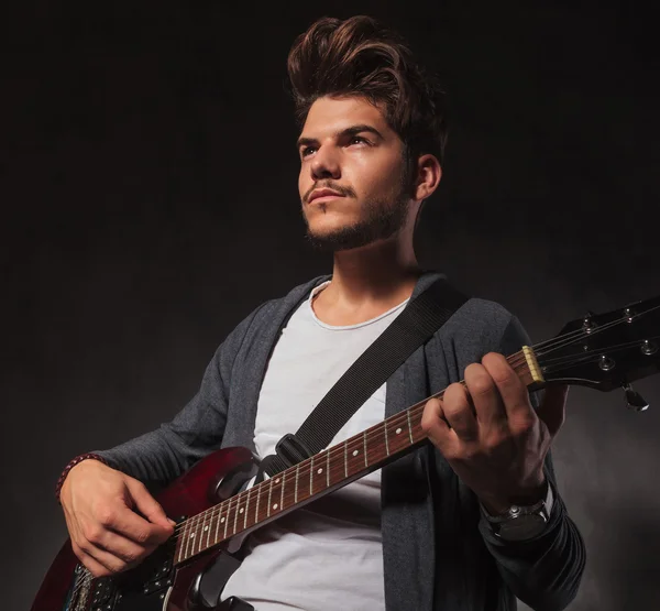 Artista tocando la guitarra en el fondo del estudio mientras mira hacia otro lado — Foto de Stock