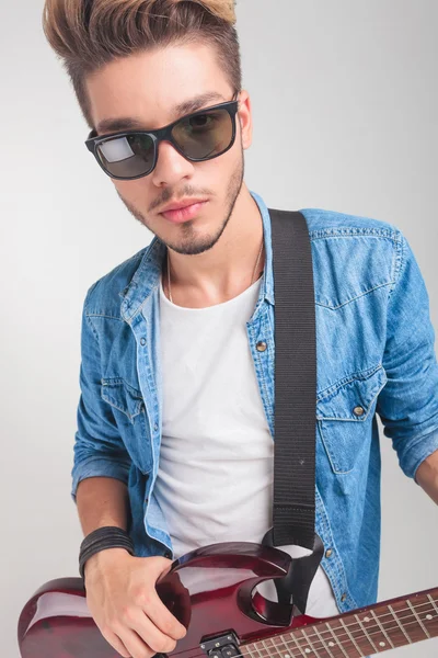 Jovem segurando uma guitarra enquanto olha para a câmera — Fotografia de Stock