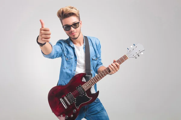 Homem em estúdio segurando uma guitarra enquanto mostra o sinal de vitória — Fotografia de Stock