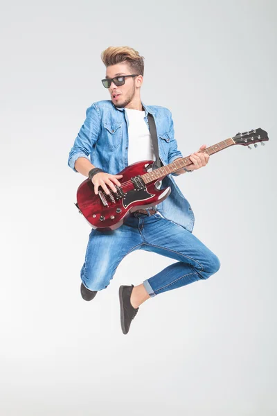 Guy wearing sunglasses jumping in studio while playing guitar — Stock Photo, Image