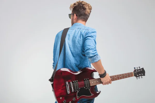 Rear view of young artist holding a guitar in studio — Stock Photo, Image