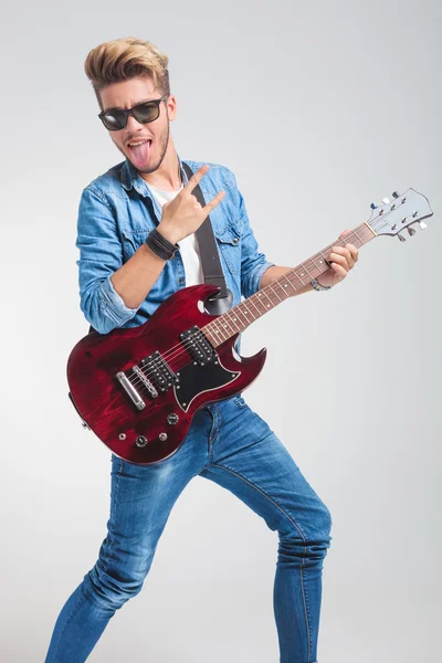 Hipster playing guitar with tongue out showing rock and roll sig — Stock Photo, Image