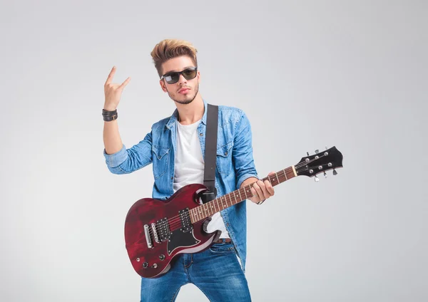 Artista posando en el estudio sosteniendo una guitarra y mostrando el rock un — Foto de Stock