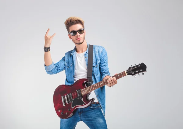 Artist posing in studio holding a guitar and showing the rock an Stock Photo