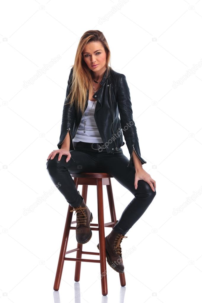 girl in boots and leather jacket pose seated in white studio bac