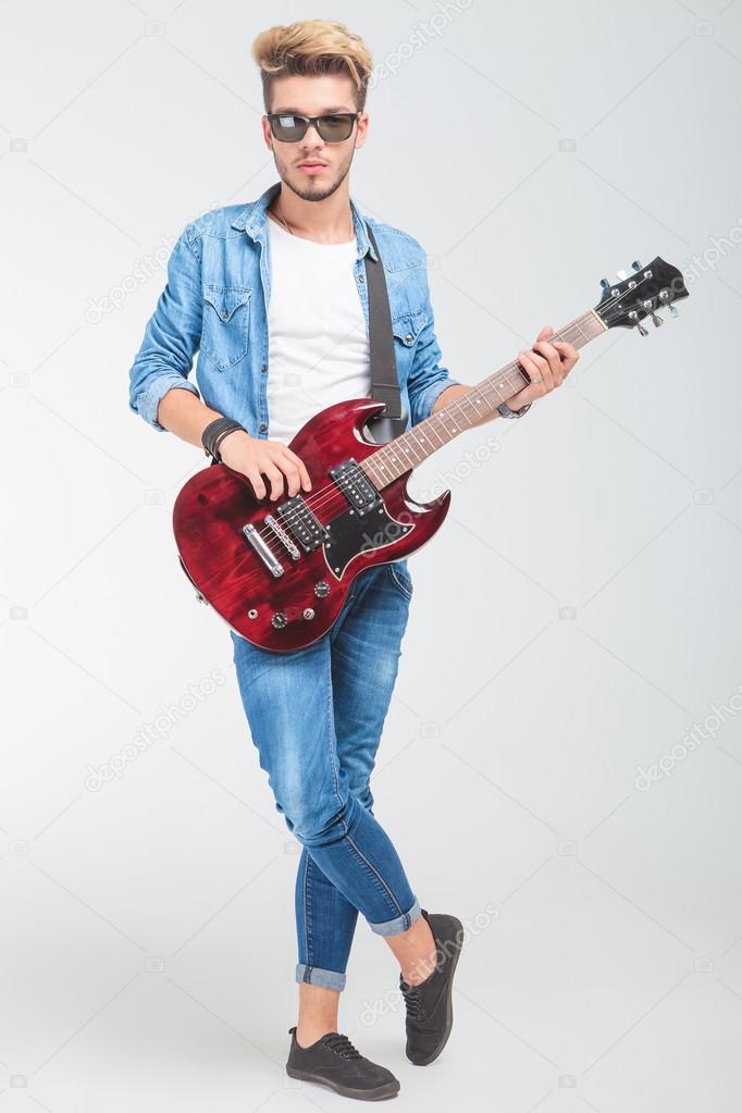 man playing guitar in studio while standing legs crossed