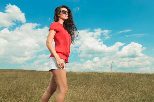 Νεαρή γυναίκα που φοράει γυαλιά ηλίου περπατώντας στους αγρούς — Φωτογραφία Αρχείου