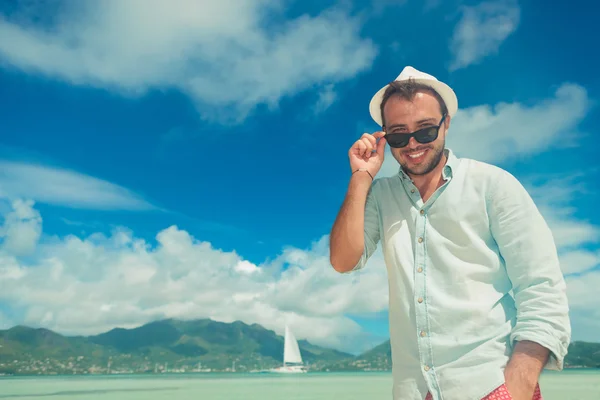 Uomo in riva al mare sorridente e fissare i suoi occhiali da sole — Foto Stock