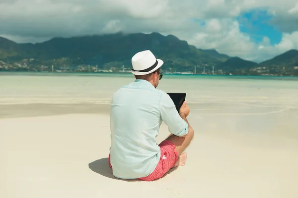 Людина в піску з ногами схрещений читання ipad — стокове фото
