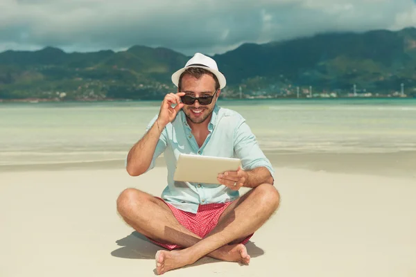 Людина з ipad на пляжі посміхається і фіксує свої сонцезахисні окуляри — стокове фото