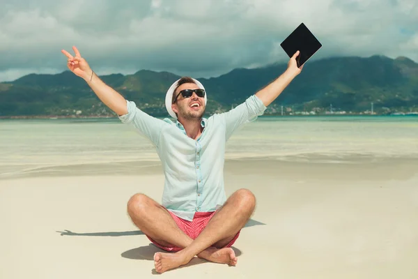 Mann im Sand zeigt Siegeszeichen und hält iPad — Stockfoto