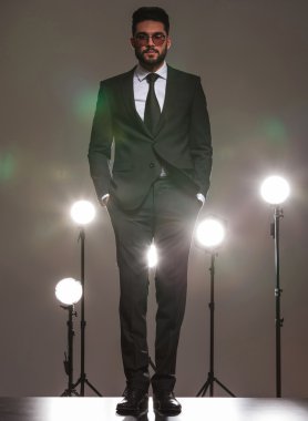 business man in black, standing in studio with hands in pockets