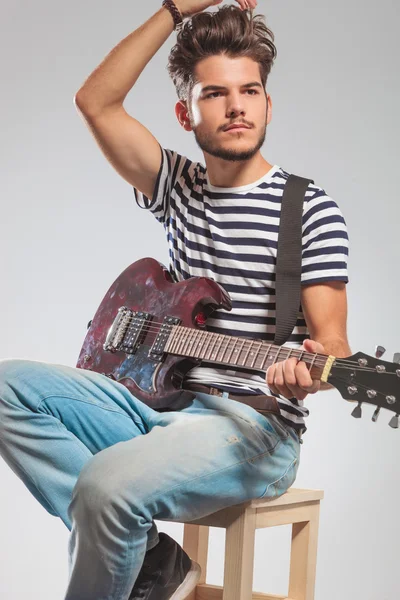 Artist playing guitar seated on chair while fixing his hair — Stockfoto