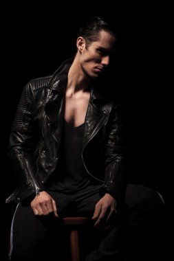 rocker in black leather jacket posing seated in dark studio